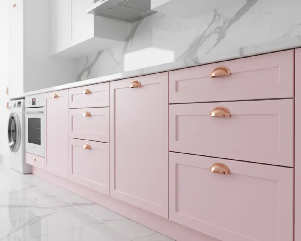 Um conjunto de gavetas em armário de cozinha na cor rosa claro com puxadores concha dourados, ideal para decoração moderna e feminina.