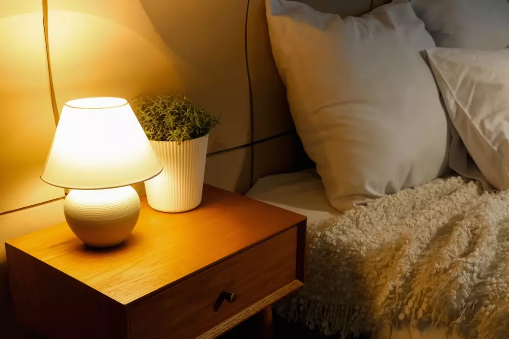 Quarto com abajur de tamanho confortável na mesa de cabeceira, iluminando suavemente o ambiente ao lado da cama com almofadas e roupa de cama confortável.