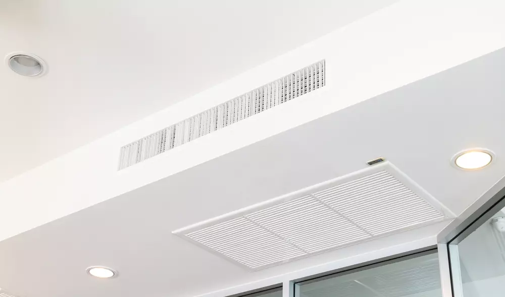 Split cassete de ar-condicionado integrado na decoração de um ambiente residencial, com paredes brancas e cortinas cinza, mostrando como integrar o aparelho na decoração.