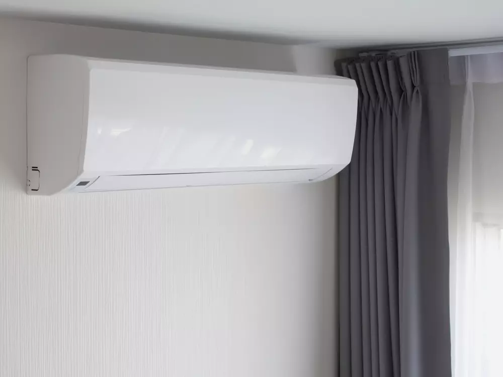Um ar-condicionado instalado na parede ao lado de cortinas cinzas.