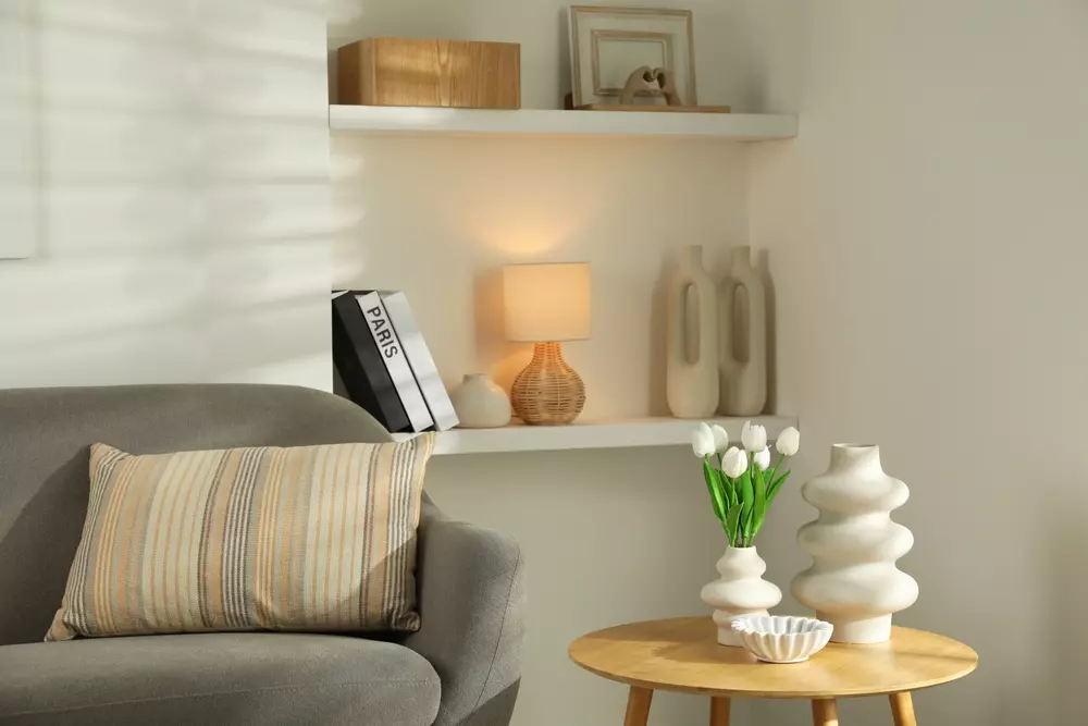 Decoração de sala de estar com vaso de tulipas brancas, mesa de madeira, sofá cinza e luminária aconchegante no fundo, criando ambiente moderno e elegante.