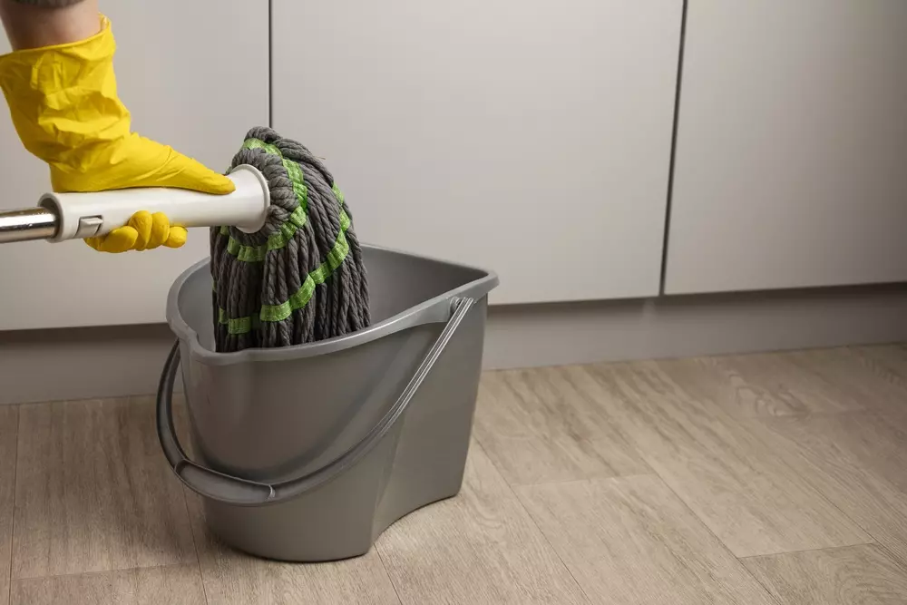 Cuidar da limpeza e higiene doméstica com balde, esfregona e luvas de borracha amarelas na cozinha moderna.