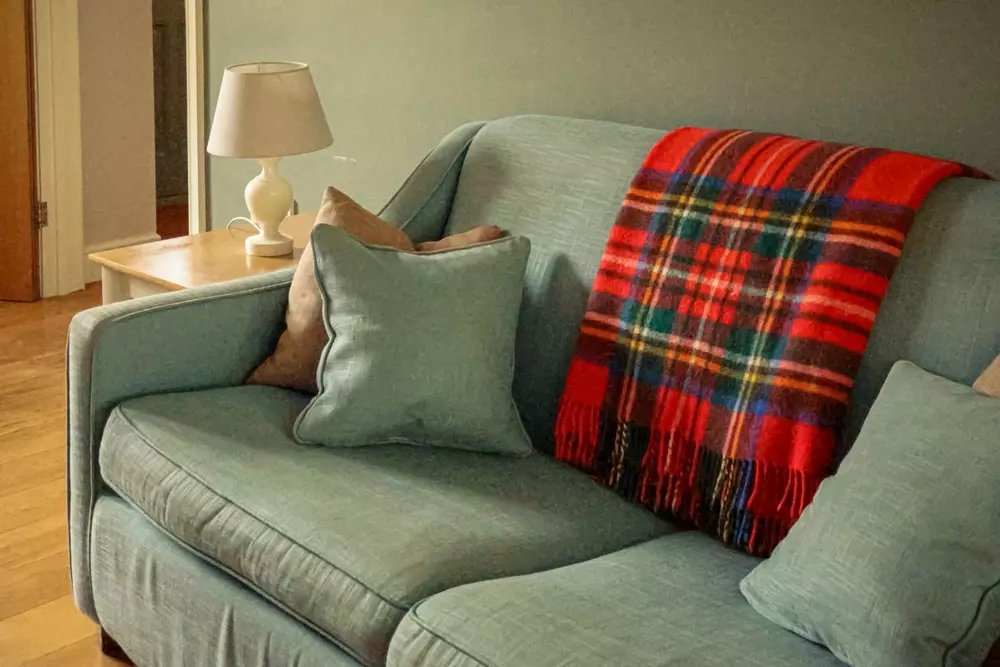 Detalhes têxteis de um charme discreto na decoração com almofadas em tom pastel sobre um sofá verde claro, decorado com uma manta xadrez em vermelho, verde e azul, criando um ambiente aconchegante e elegante.