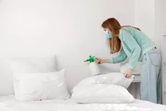 Mulher usando máscara e spray para controlar o mofo em travesseiro na cama