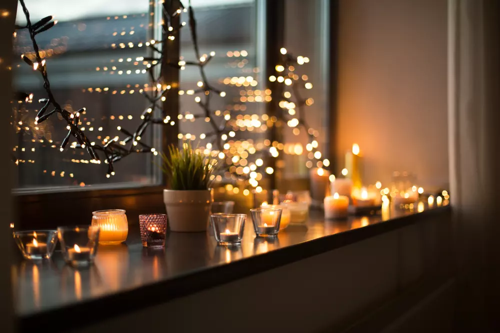Decoração aconchegante na janela com velas acesas e luzes, criando uma atmosfera de 'bagunça boa' que traz conforto e bem-estar ao ambiente.