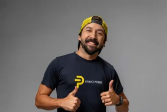 Eduardo Feldberg, sorridente usando camisa com logotipo 'Primo Pobre' e boné amarelo