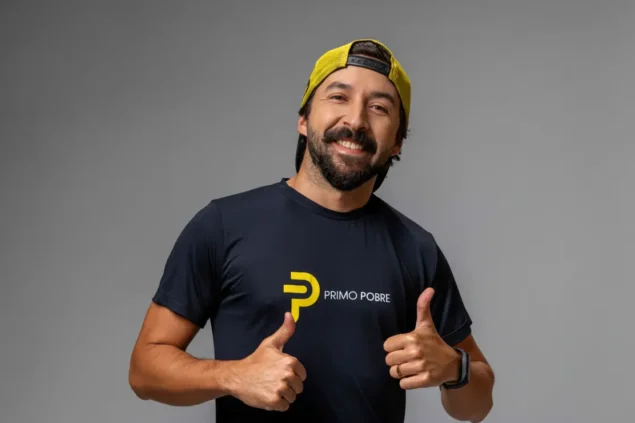 Eduardo Feldberg, sorridente usando camisa com logotipo 'Primo Pobre' e boné amarelo