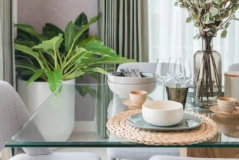 Mesa de jantar moderna com tampo de vidro, decoração com plantas e utensílios de louça