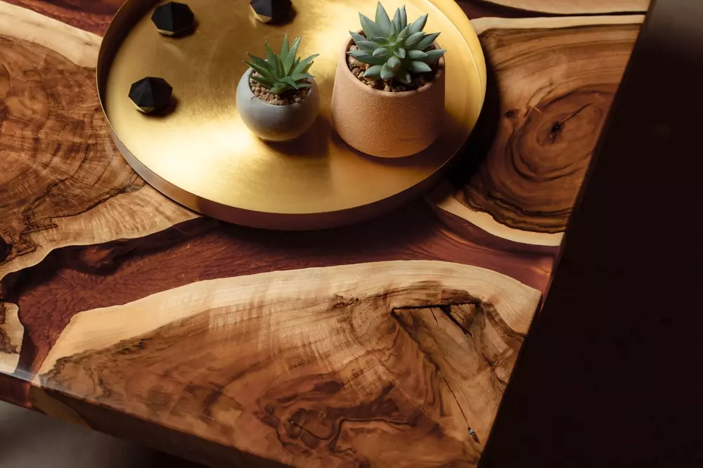 Tampo de mesa de madeira com acabamento rústico, decorado com uma bandeja dourada, plantas suculentas e pequenos objetos decorativos.