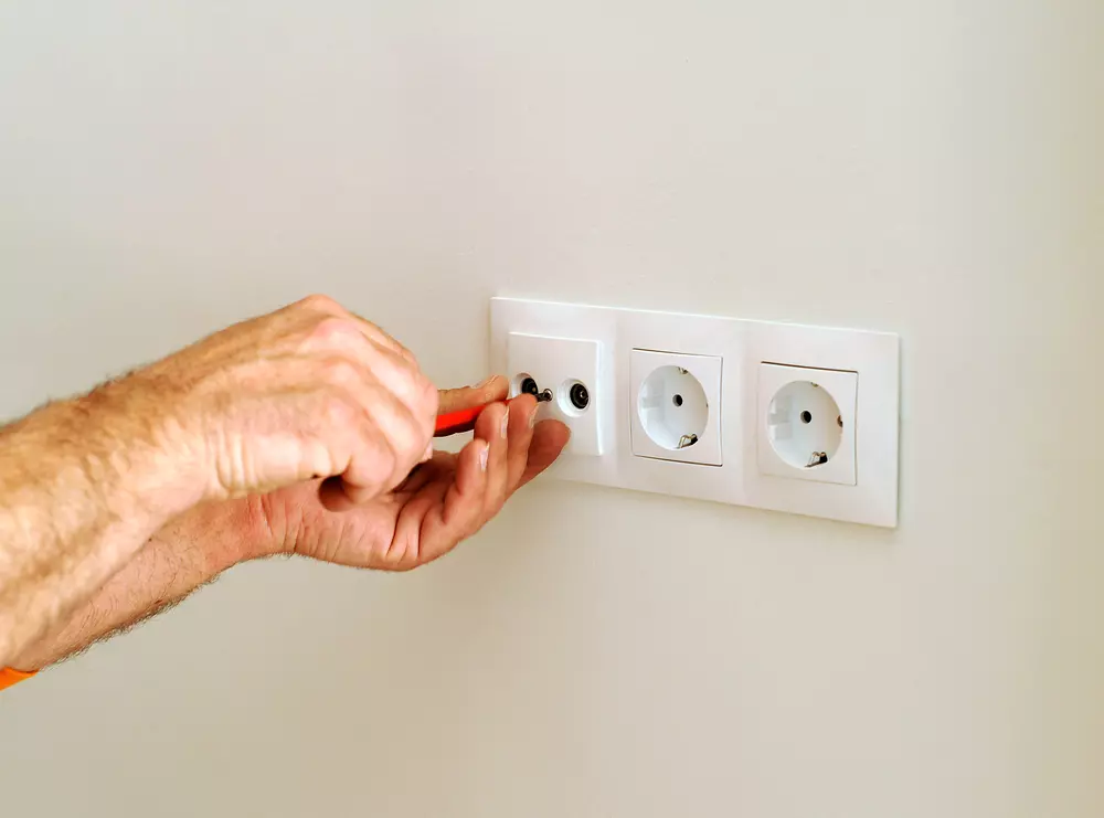 Instalação de adaptadores e multiplicadores em excesso em tomadas elétricas, mostrando a conexão de cabos na parede.