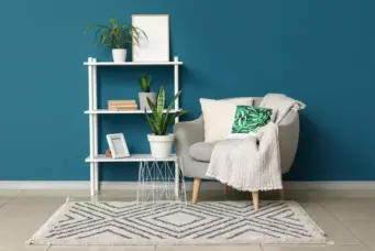 Decoração moderna com parede azul vibrante destacando a cor do ano 2026, sofá cinza claro, almofadas verdes e uma estante branca decorada com plantas e livros.