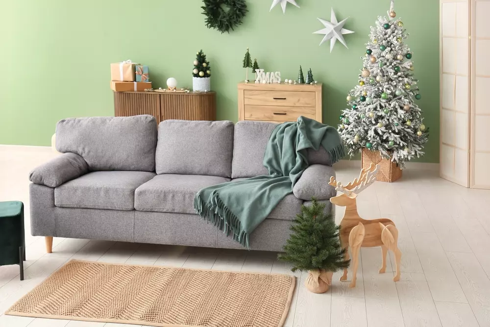 Decoração de Natal minimalista com cores neutras e suaves, incluindo uma árvore de Natal decorada, presentes, uma árvore de pinho pequena, enfeites de Natal e uma sala aconchegante com sofá cinza e decoração discreta.