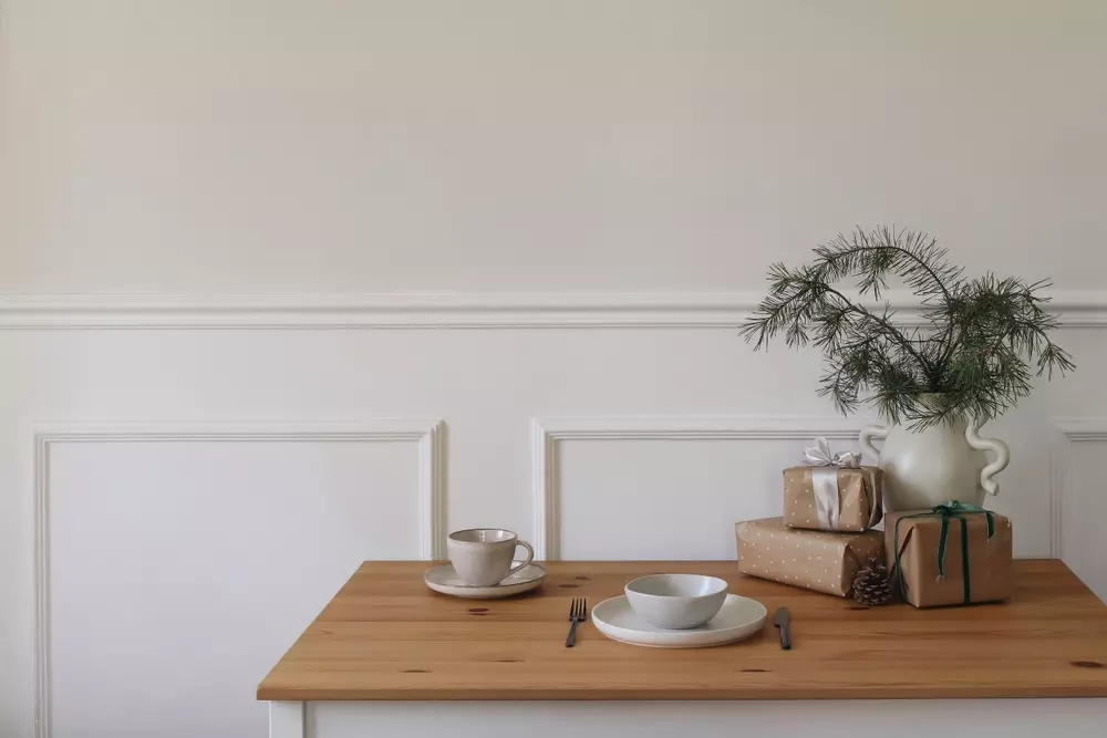 Mesa de jantar decorada com presentes e uma jarra com galhos de árvore, sugestiva de preparação para celebração