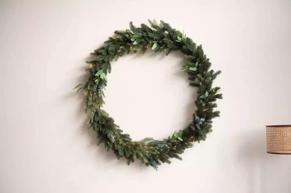Guirlanda de Natal feita com galhos verdes e folhagens, decorada de forma simples e elegante na parede.