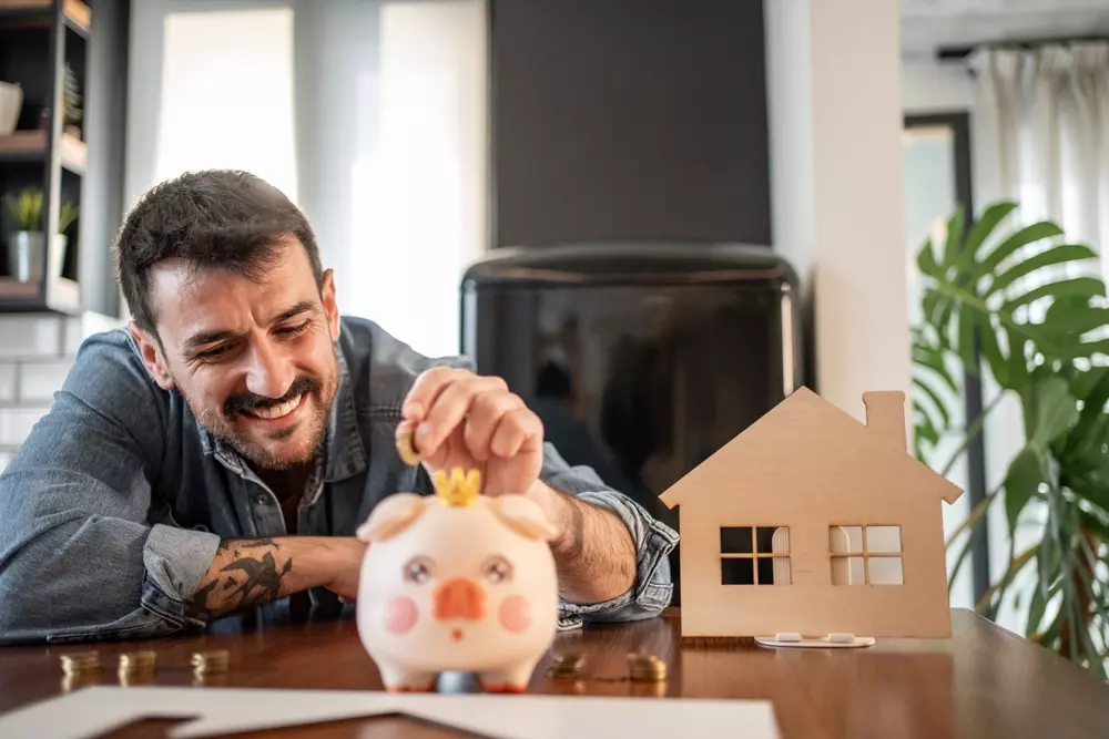 homem sorrindo enquanto coloca moeda em seu cofrindo para conquistar seu sonho