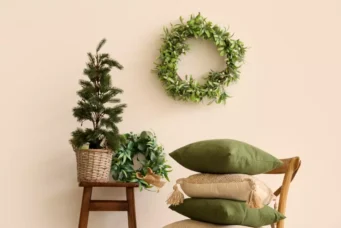 Decoração de Natal minimalista com plantas verdes, uma coroa de hera na parede, almofadas verdes e uma cadeira de madeira, criando um ambiente simples e elegante.