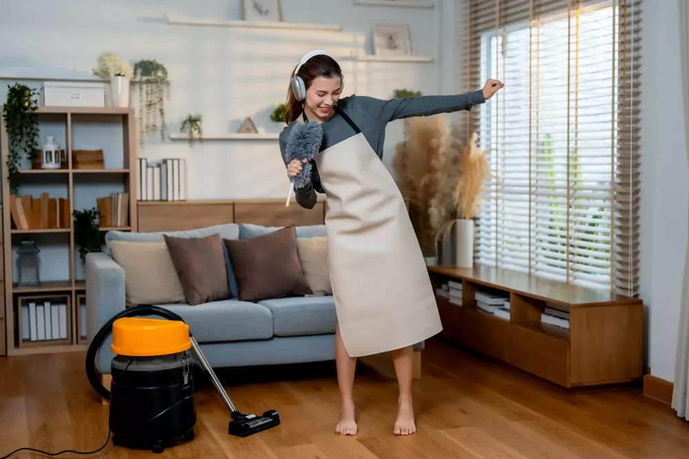 Mulher com fone de ouvido e dançando em casa, com ambiente confortável e iluminação natural.