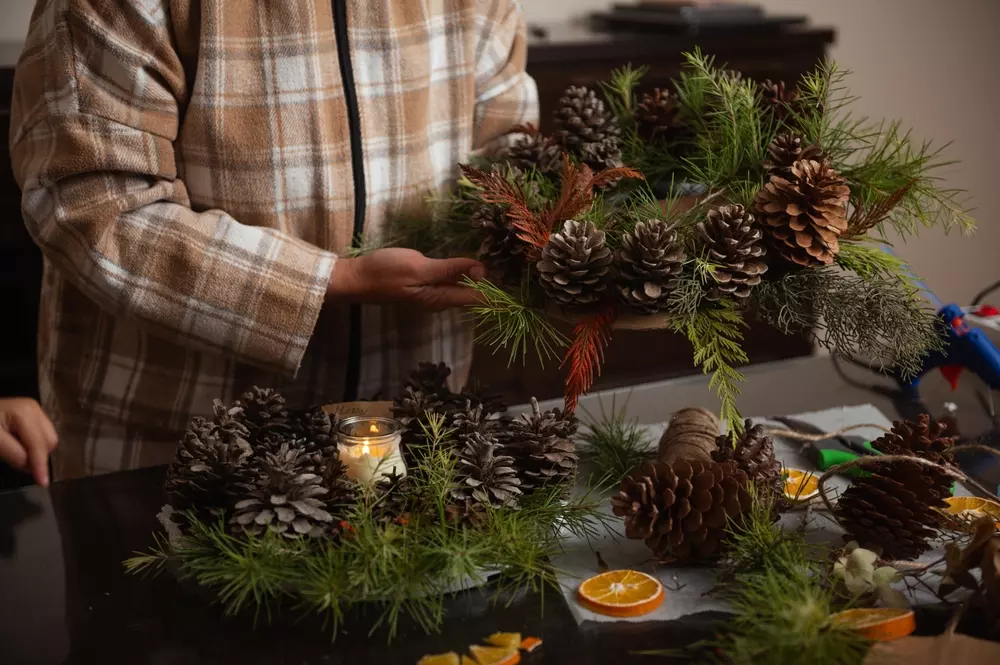 Pessoa criando decoração de Natal rústica e woodland com pinhas, folhagens verdes e elementos naturais para tendências de Natal 2025