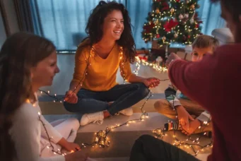 Família celebrando Natal com decoração moderna e iluminação aconchegante, tendência de decoração de Natal 2025 com árvore decorada ao fundo.