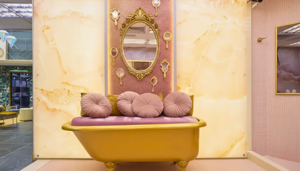 Decoração retrô contemporâneo BBB26 com sofá dourado, almofadas pink e detalhes elegantes em espelho e rosa na parede.