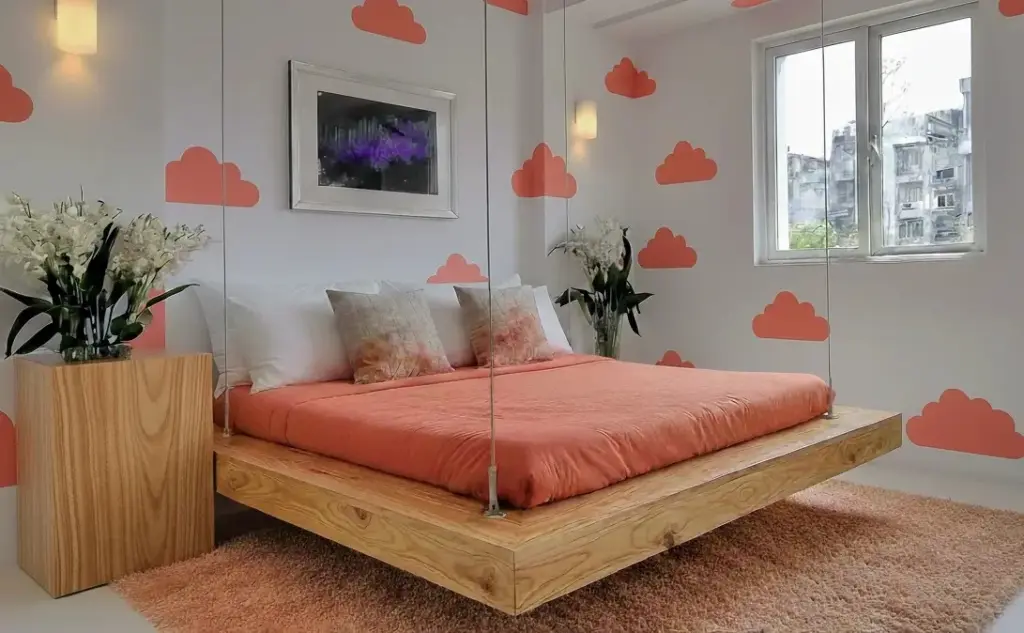 Quarto decorado com cama suspensa de madeira, paredes com ilustrações de nuvens na cor coral, janelas com vista urbana
