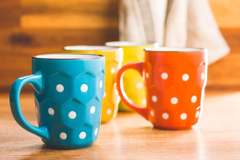 Conjunto de três canecas de cozinha coloridas com padronagem de poás, ideal para o café da manhã ou chá, em uma cozinha com fundo de madeira.