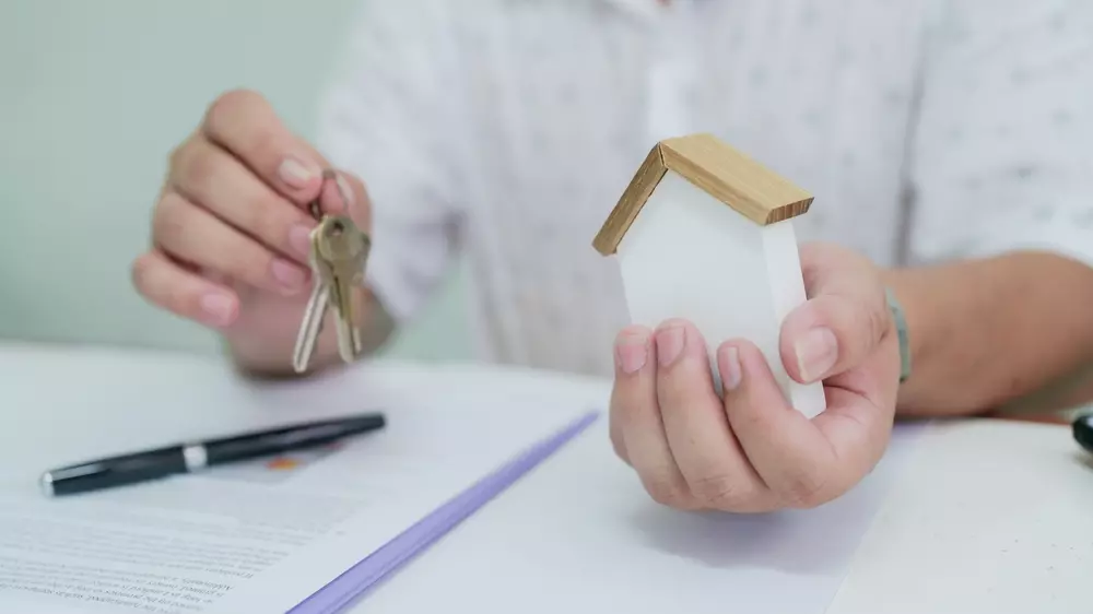 Pessoa segurando chave e uma maquete de casa, simbolizando pagamento de IPTU em duplicidade, problema comum em processos de pagamento de impostos.