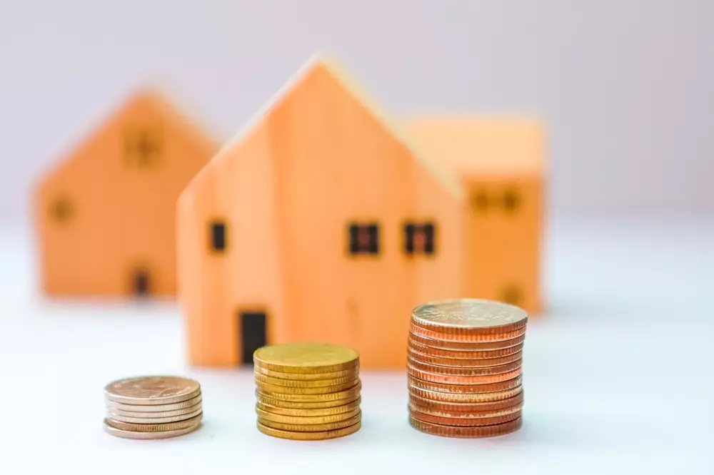 Casas de MDF em miniatura e pilhas de moedas, representando o impacto da Selic alta na compra de imóvel.