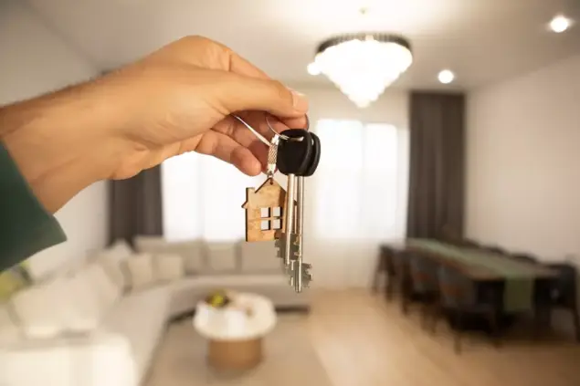 Chave de apartamento com símbolo de uma casa de madeira, segurada por mão, em ambiente de sala de estar moderna, simbolizando pagamento de IPTU em duplicidade.