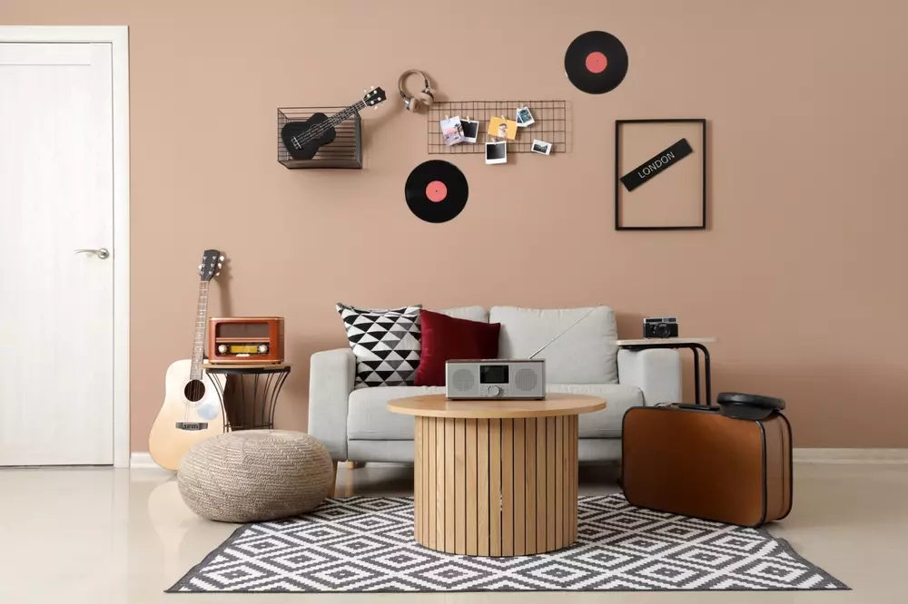 Ssala de estar moderna com parede rosa, decorada com discos de vinil, fotos, um sofá branco com almofadas, violões, uma mesa redonda de madeira, e uma cômoda.
