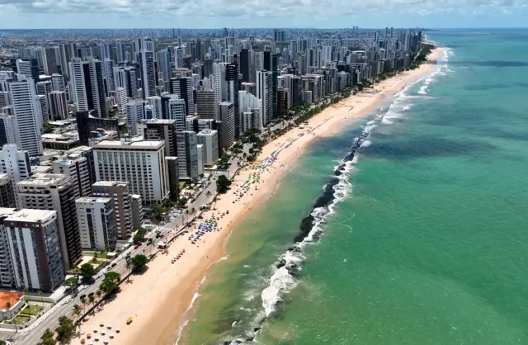 Vista aérea do litoral de uma cidade moderna de Pernambuco, com arranha-céus altos ao longo da orla, praias de areia dourada e mar azul oceano, destacando as melhores cidades de Pernambuco para morar.