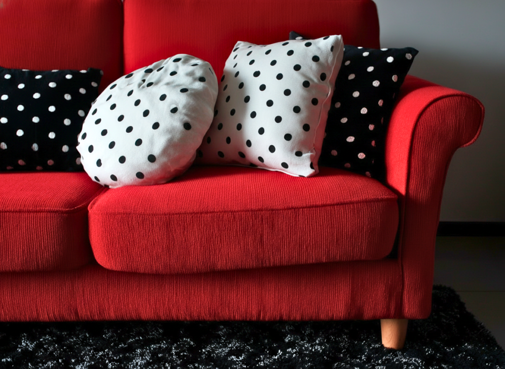 Sofá vermelho decorado com almofadas de poá em branco e preto.
