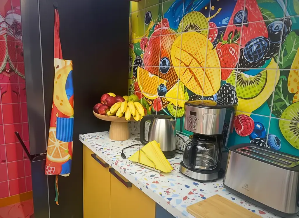 Cozinha do BBB 26 com parede decorada de frutas coloridas, mostrando ambiente vibrante e moderno