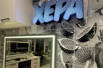 Cozinha do BBB 26 decorada com detalhes em preto, branco e cinza, destaque para o painel com o nome 'Xepa' iluminado e uma parede com azulejos modernos.