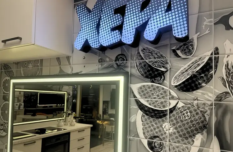 Cozinha do BBB 26 decorada com detalhes em preto, branco e cinza, destaque para o painel com o nome 'Xepa' iluminado e uma parede com azulejos modernos.