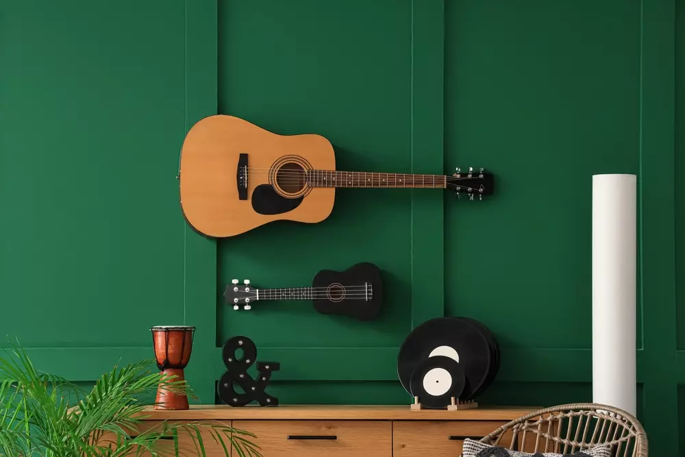 Decoração com instrumentos musicais, guitarra acústica e ukulele na parede verde, decorando um ambiente moderno e criativo.