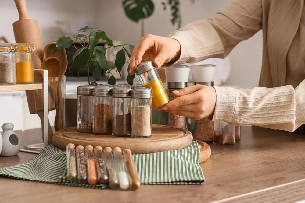 Pessoa organizando temperos e especiarias em potes na cozinha, destacando ingredientes utilizados na culinária
