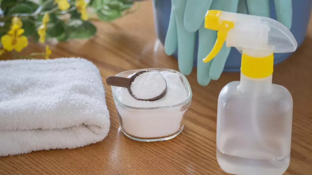 Itens de limpeza caseira incluindo uma luva de borracha, uma tigela com bicarbonato de sódio, uma esponja, e um spray de limpeza, ideal para manutenção doméstica.