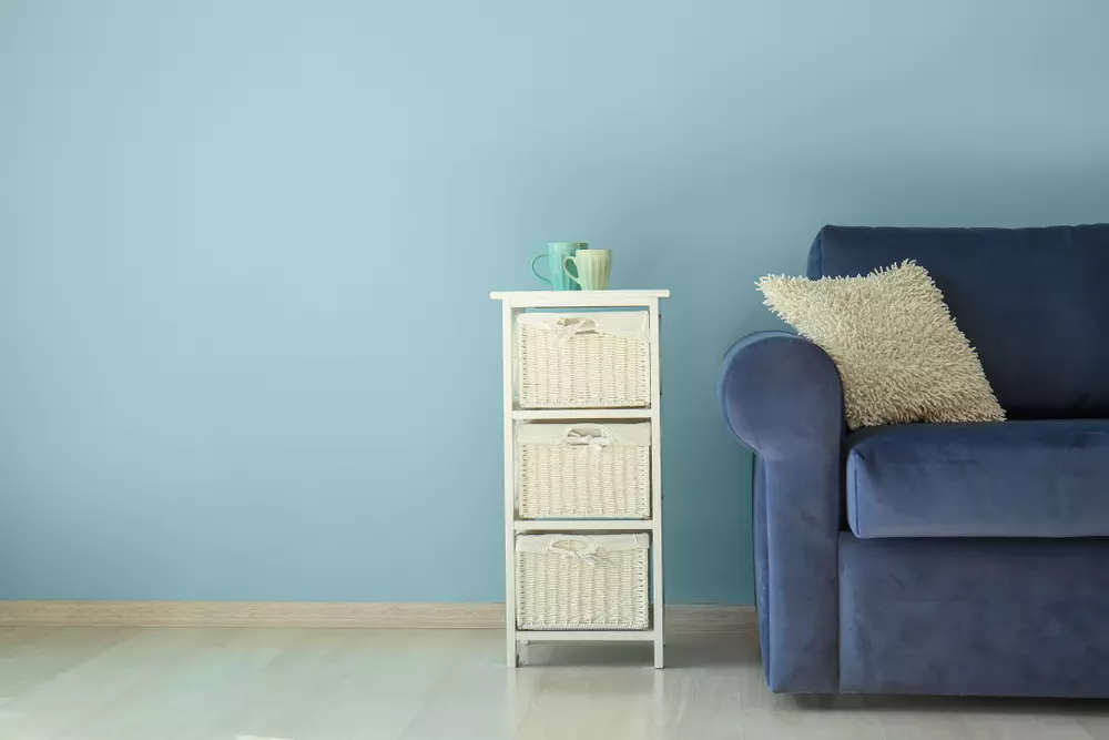 Móveis coloridos, incluindo uma cômoda branca com cestas e um sofá azul com almofada bege, em uma sala decorada de forma moderna.