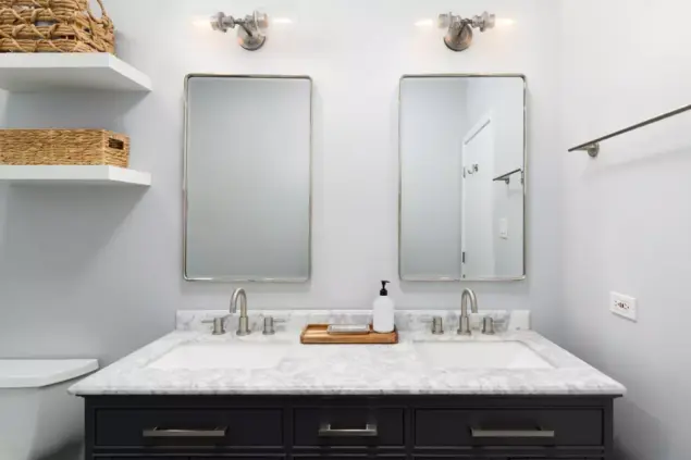 Um banheiro organizado com espelhos, pia de mármore, prateleiras com cestarias e iluminação bem distribuída, ideal para otimizar o espaço.