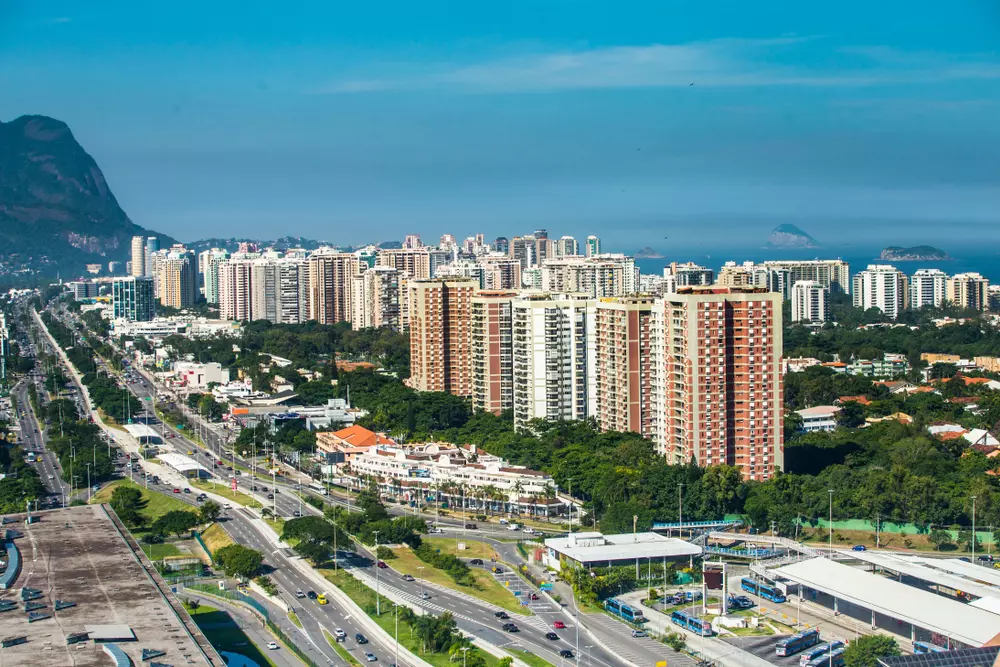 Panorâmica da Barra da Tijuca no Rio de Janeiro, com altos edifícios, vias movimentadas e a natureza ao redor, destacando a beleza urbana e litoral da região.