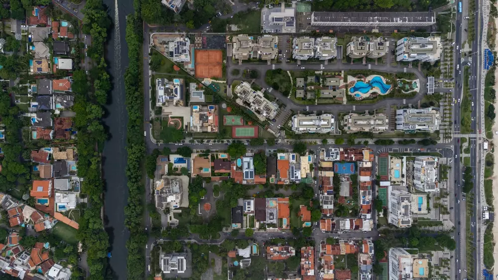 Vista aérea da Barra da Tijuca, bairro do Rio de Janeiro, mostrando condomínios residenciais, áreas verdes, piscina e ruas estruturadas, destacando a diversidade de ambientes urbanos e residenciais.