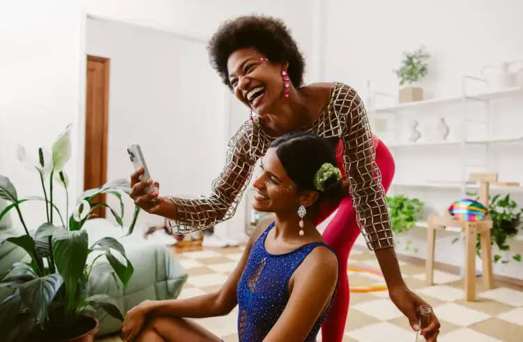Duas mulheres felizes no interior de uma casa decorada para o Carnaval, com decoração colorida e alegre, celebrando a renovação para a festa.