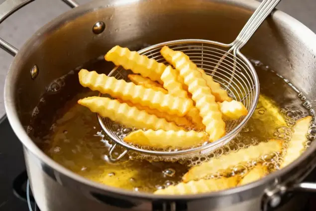 Uma panela com óleo fritando batatas em palitos. Ilustrando matéria sobre eliminar cheiro de fritura da casa.