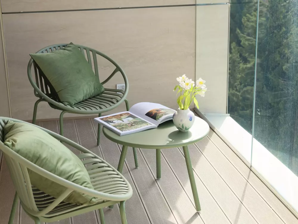 Um espaço de varanda decorado com cores de 2026, incluindo móveis em tom de verde suave, com almofadas em verde, uma mesa com vaso de flores brancas.