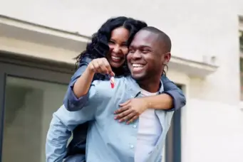 Faixa 4: como planejar a entrada sem travar outros sonhos? Na foto casal feliz segurando as chaves da casa, celebrando a conquista com um sorriso radiante e alegria, simbolizando sucesso e realização.