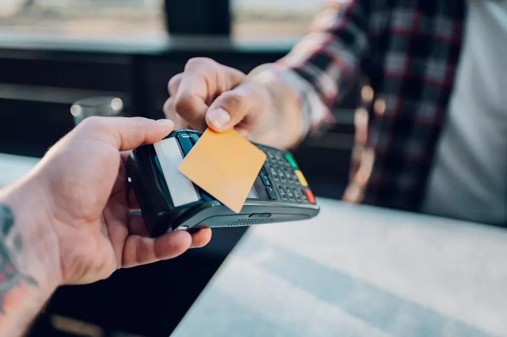 Pessoa realizando pagamento com cartão de crédito em um leitor eletrônico, destacando a importância do cartão de crédito para compras e transações financeiras.