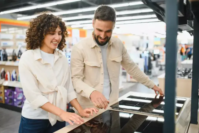 Casal em uma loja de eletrodomésticos olhando modelos de cooktops para decidir se irá optar por usar em sua casa cooktop ou fogão.