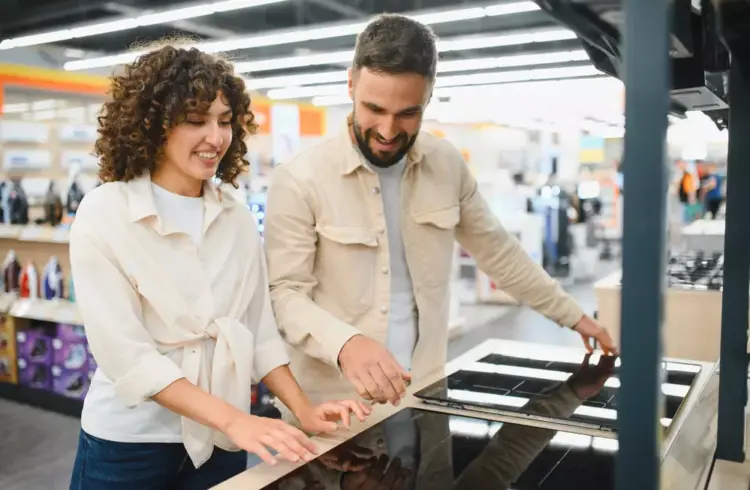Casal em uma loja de eletrodomésticos olhando modelos de cooktops para decidir se irá optar por usar em sua casa cooktop ou fogão.