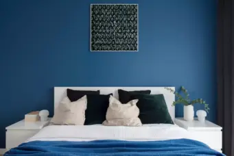 Decoração de quarto moderno com cores de 2026, destaque para parede azul, roupas de cama em tons neutros, com detalhes em verde e branco, criando ambiente sofisticado e aconchegante.